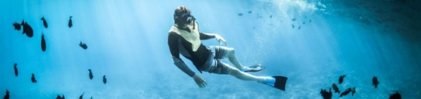 Snorkel expert enjoying his adventure at the bottom of sea with the little fishes around him